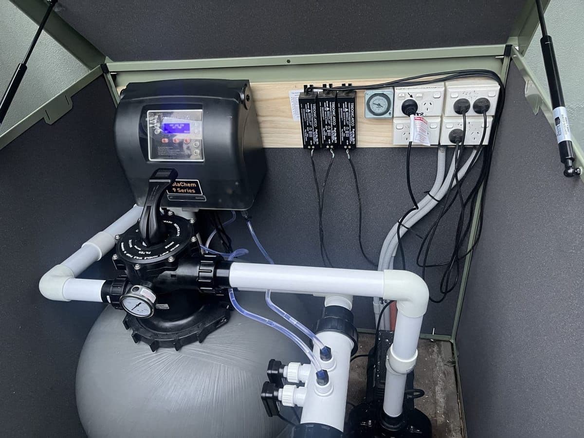 Inside a pool equipment enclosure, with a sand filter, chlorinator and new PVC pipework mounted on a backboard