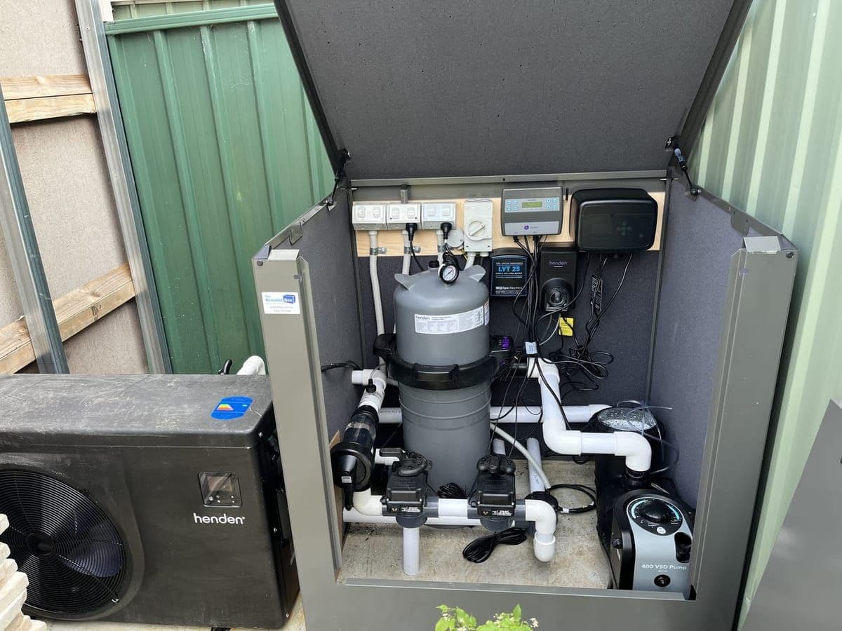 Outdoor pool equipment bay with a heat pump beside a cartridge filter and a variable-speed pump inside an acoustic enclosure